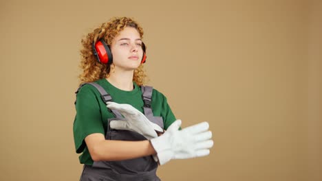 young woman in work overalls with protective earmuffs and gloves