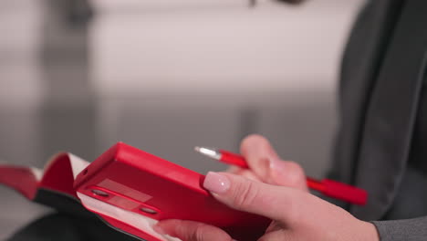 close-up of person holding red phone with one hand and using red pen to write in notebook with other hand. focus on professional work, ideal for office tasks, meetings, and brainstorming sessions
