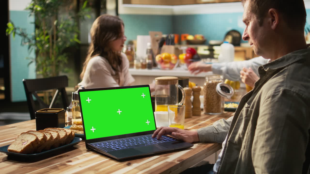 Chroma key on laptop next to mother enjoying breakfast at the kitchen table