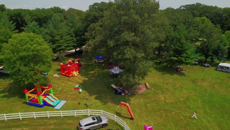 aerial view of a lush green park area featuring colorful inflatable bounce houses and playground equipment, surrounded by trees and picnic spots for family enjoyment