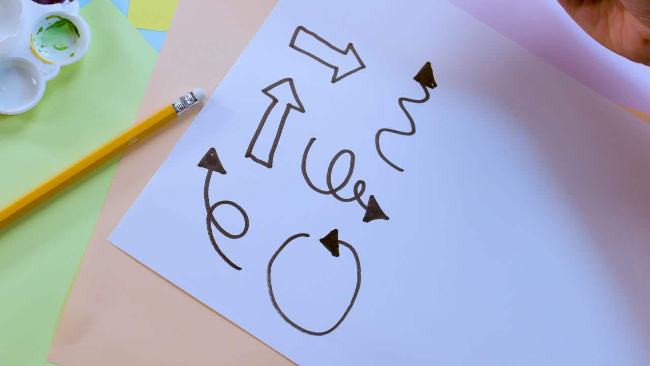 Person draws various arrows and swirls on paper with marker, top-down view, bright lighting