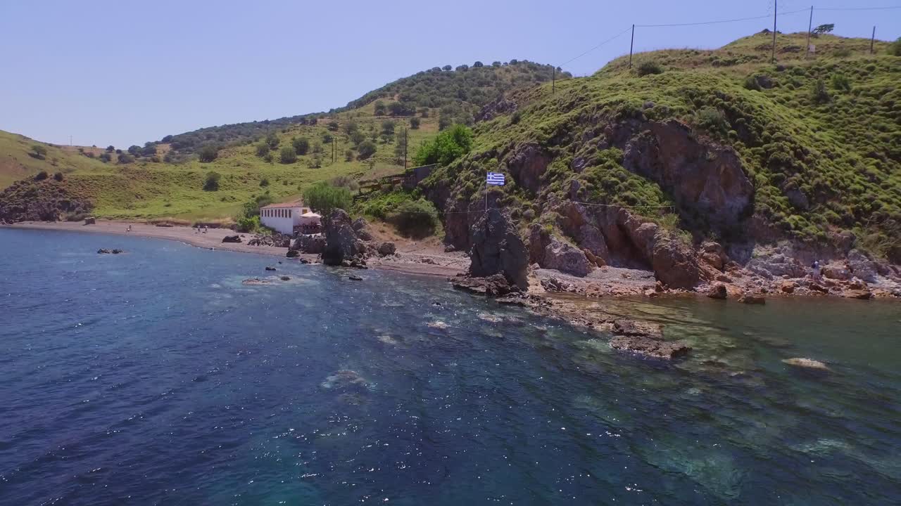 Aerial: A Greek flag on a rock waving the wind on the island of Lesbos, Greece