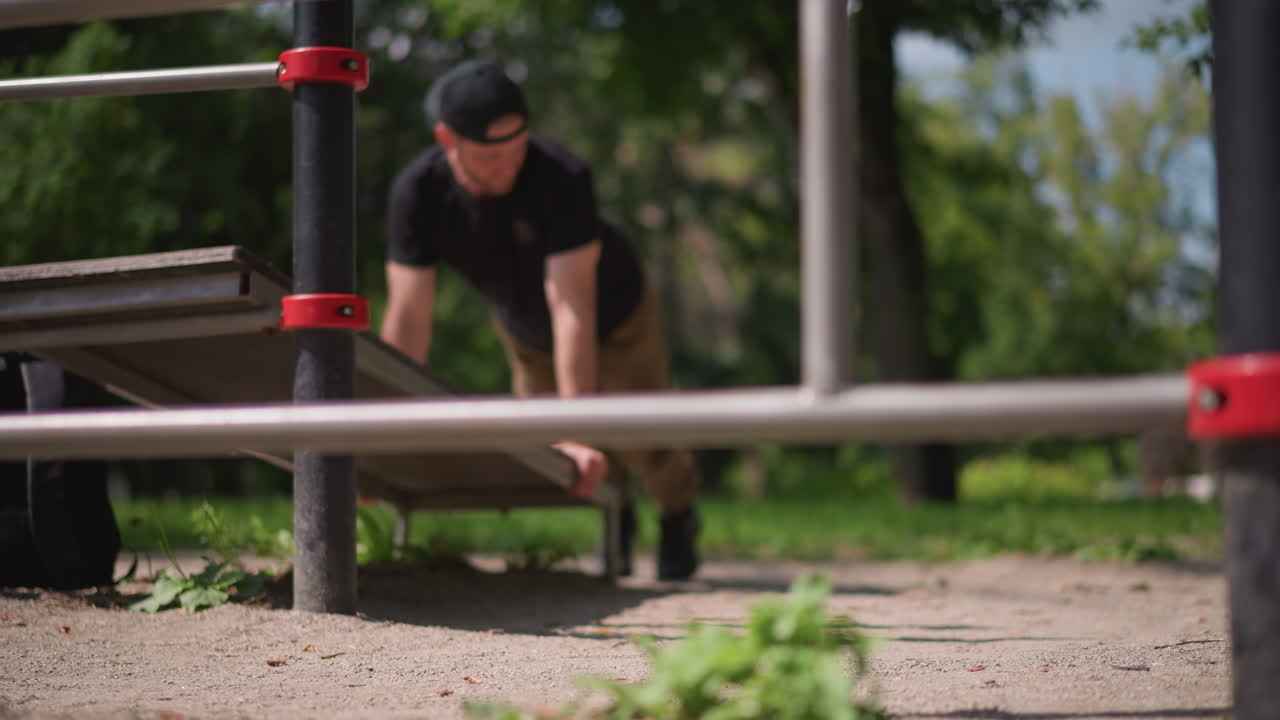 Athlete Packing Outdoors, Runner Crouching To Retrieve Backpack Under Bench In Park Setting, Sports Enthusiast Kneeling To Access Gear Beneath Bench Amid Leafy Park Environment With Sunlight