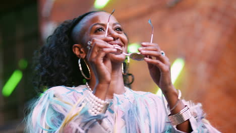 young black woman wearing multicoloured fringed jacket putting on sunglasses, low angle, head and shoulders