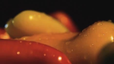 macro shot of fresh colorful banana peppers and water drops rotating in front of black background