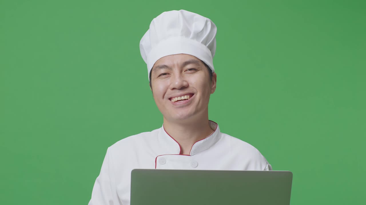 Close Up Of Asian Man Chef Using A Laptop And Smiling To Camera While Standing In The Green Screen Background Studio