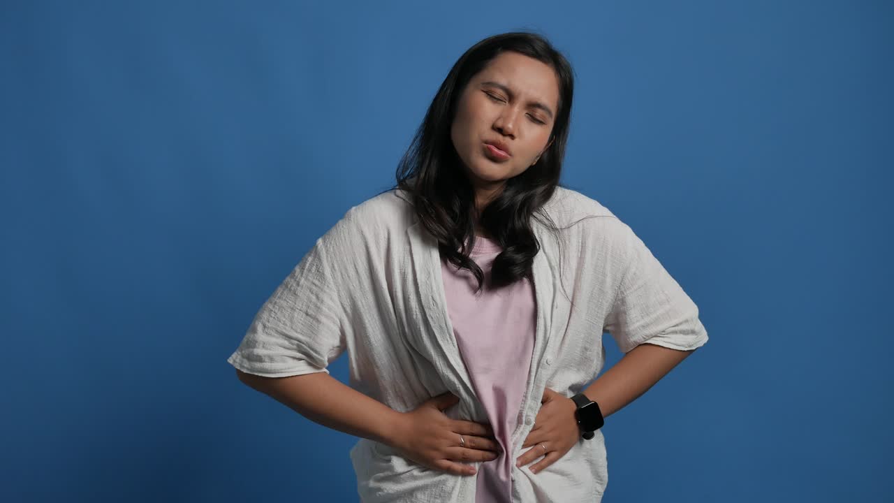 Young asian woman suffering for stomach ache standing over isolated blue background