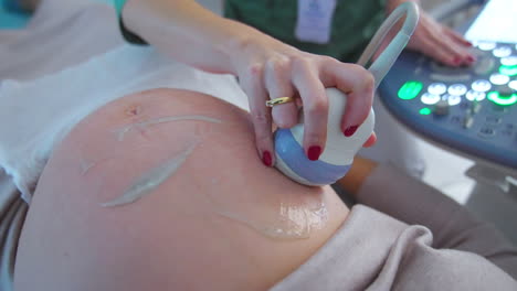 hand of a doctor holding ultrasonic device moves by the big pregnant belly of a patient. close up. ultrasound check up concept.