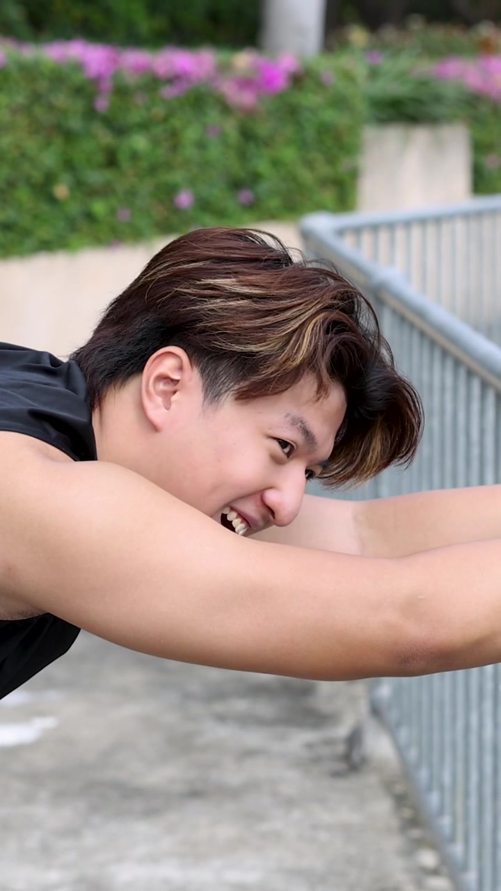 A fit young man performs deep back and shoulder stretches using a metal park railing.
