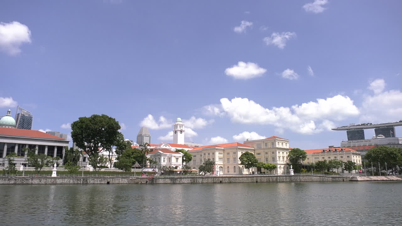Time lapse footage of the Singapore River in Boat Quay on a sunny afternoon with a tourist ferry passing by, clear sky, asian civilization museum, marina bay sands.