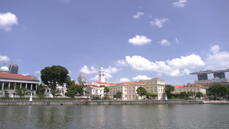 time lapse footage of the singapore river in boat quay on a sunny afternoon with a tourist ferry passing by, clear sky, asian civilization museum, marina bay sands.