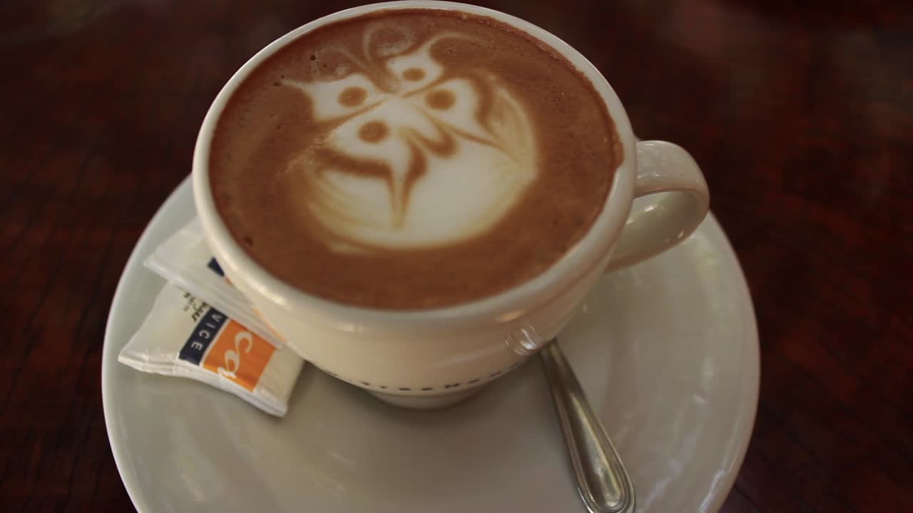 Mani che posizionano una tazza di caffè con latte art su un tavolo di legno
