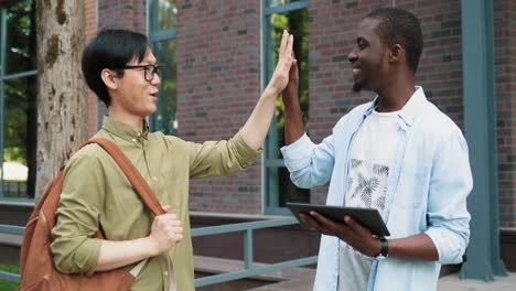 african american student using tablet in the street near the college