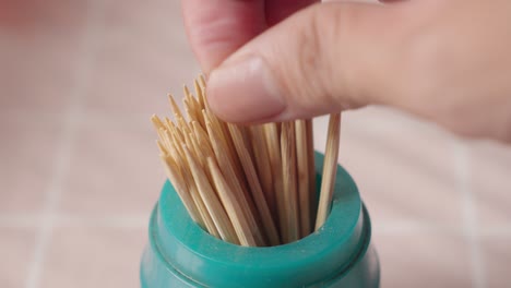 hand picking up a wooden toothpick from a canister