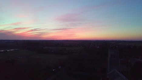 drone shot of beautiful pink sky tracking down to show rural english village with big church and graveyard