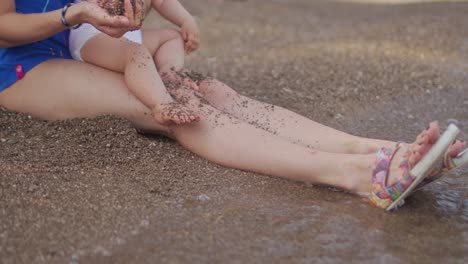 mother and daughter sitting on the beach and play with sand