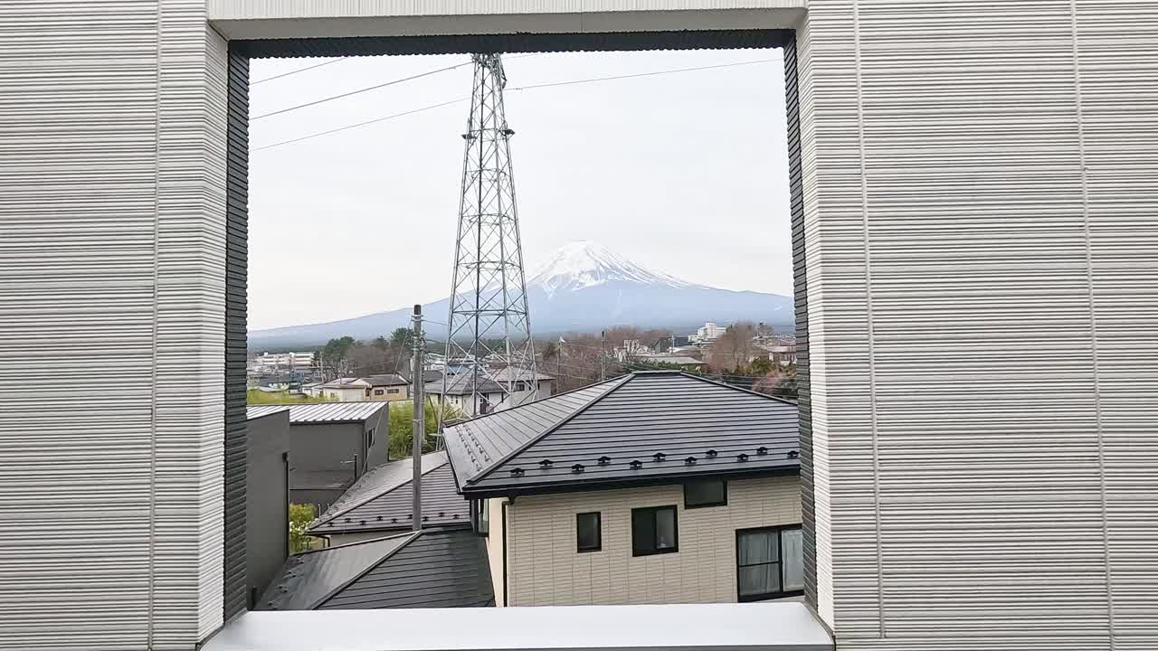 una vista serena del monte fuji enmarcada por una ventana en kawaguchiko, japón, con cielos nublados y techos residenciales