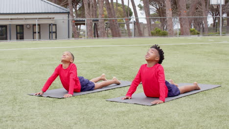multiracial boys practicing yoga on mats on school field, enjoying exercise and fresh air