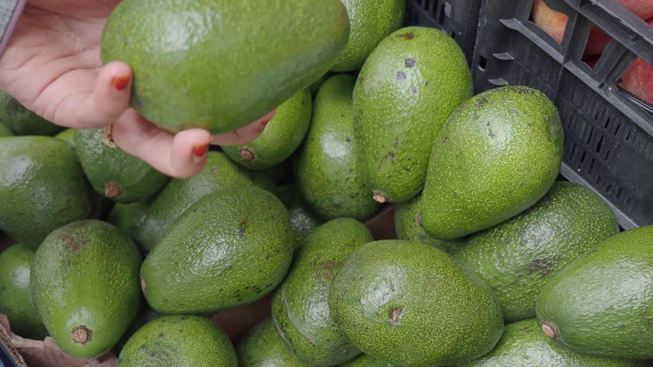 una mujer comprando aguacates en un mercado