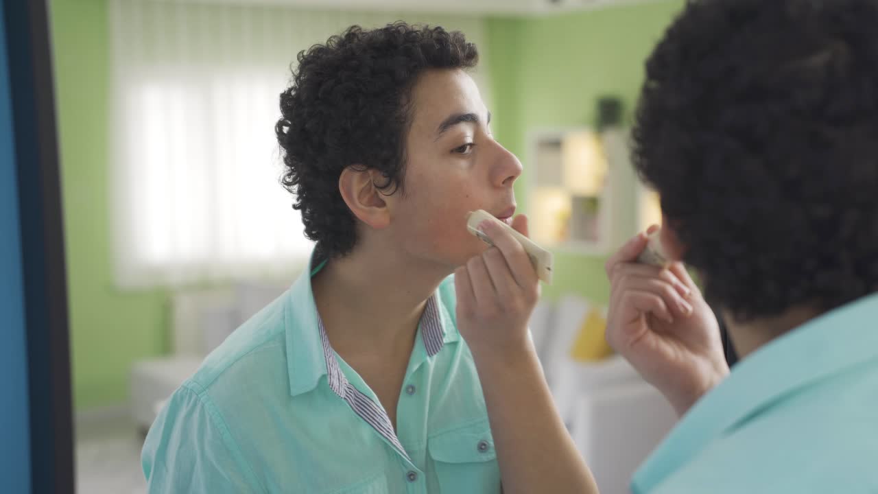 Ragazzo divertente e carino che si prende cura della sua persona si applica la crema sul viso.