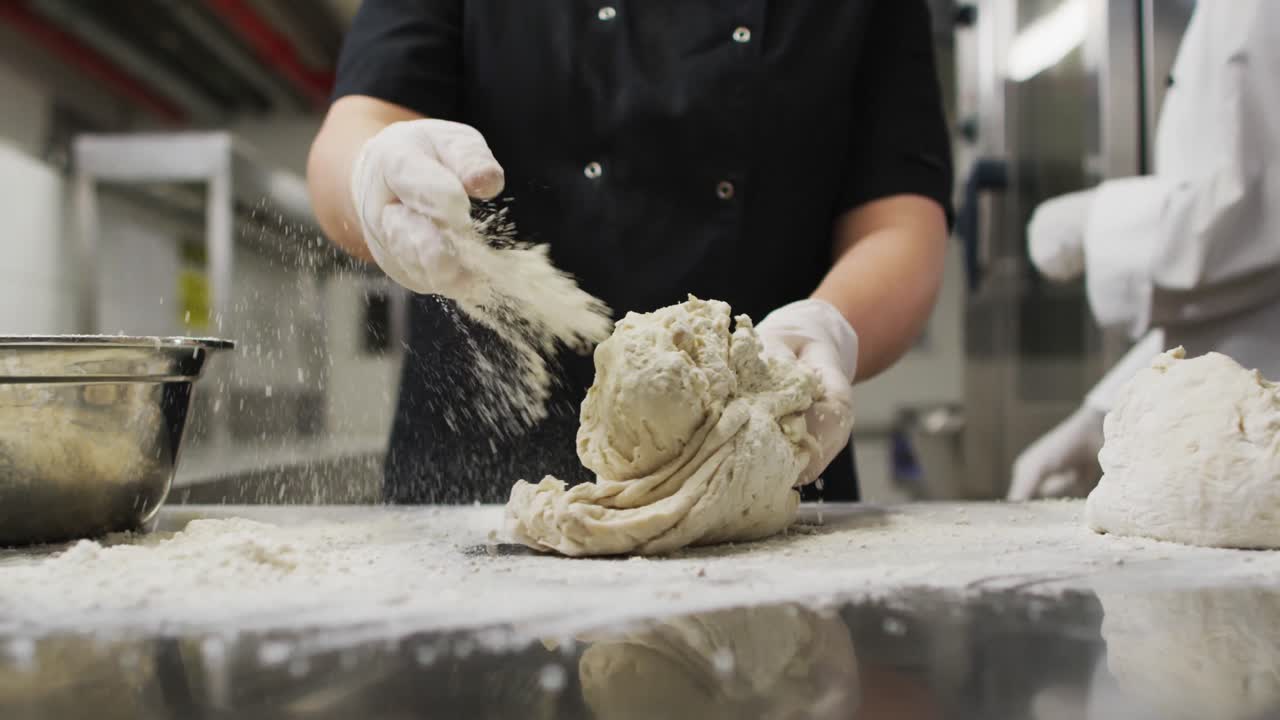 Midsection of caucasian female chef wearing rubber gloves and preparing dough
