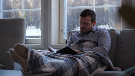 person sits in couch researching genealogy, reads book about family history