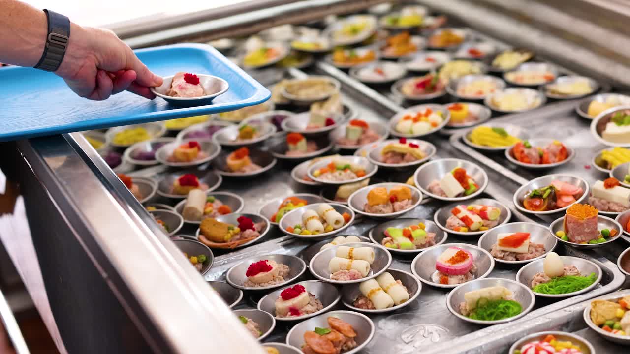 A person selects dim sum from a variety of colorful options in a well-lit market setting in Phuket, Thailand
