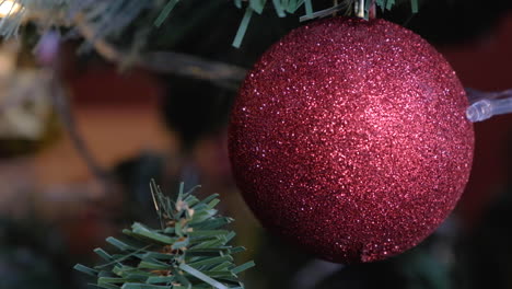 leuchtend rote weihnachtskugel auf baum mit verschwommenem lichthintergrund platziert