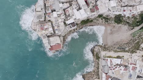 Imágenes-Aéreas-De-Arriba-Hacia-Abajo-De-Las-Olas-Rompiendo-Contra-Las-Rocas-Y-La-Costa-En-Polignano-A-Mare,-Italia,-En-Un-Día-Tormentoso