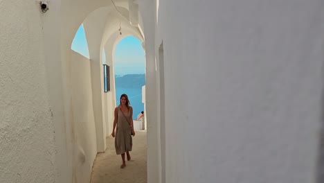 woman walks through a narrow alley between houses on the greek island of santorini