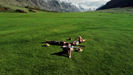 three attractive girls lying on green grass and having fun on a meadow sunny day and background of mountain