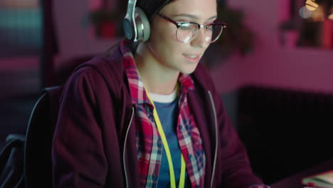 young caucasian business woman student working late using computer typing research project browsing online brainstorming deadline in trendy office at night listening to music wearing headphones