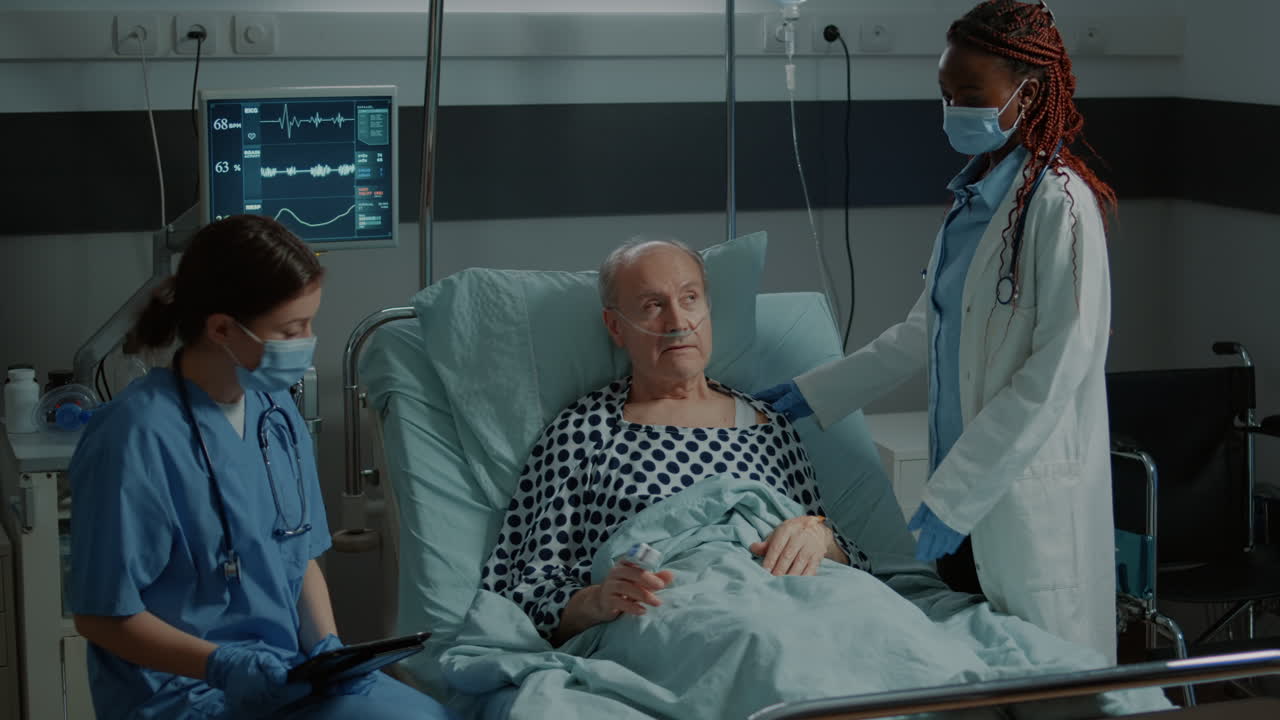Nurse with tablet advising sick patient in hospital ward bed