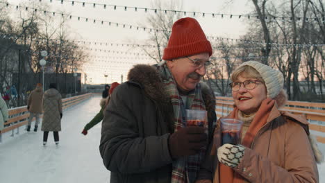 happy senior couple enjoying warm drinks at a winter ice rink