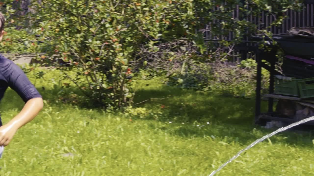 Children laugh and spray cold water with garden hosepipe in hot summer Slow-mo