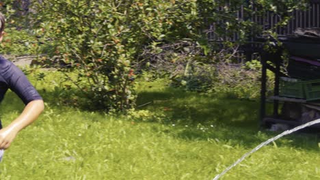 children laugh and spray cold water with garden hosepipe in hot summer slow-mo