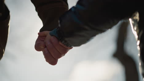 a close-up of an adult and a child holding hands, gently illuminated by the soft glow of sunlight, as the camera moves towards the boy