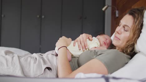 video of happy caucasian mother sleeping on bed with newborn baby