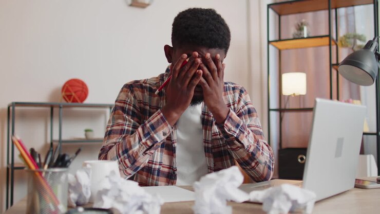Angry furious man working at home office throwing crumpled paper, having nervous breakdown at work