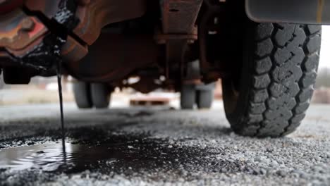 a vehicle is parked on a gravel surface with oil leaking from underneath. the dark liquid creates ripples in the puddle on the ground. this situation indicates a potential mechanical issue.