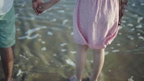 Close-up-shot-of-the-backside-of-a-couple-holding-hands-with-waves-in-the-background