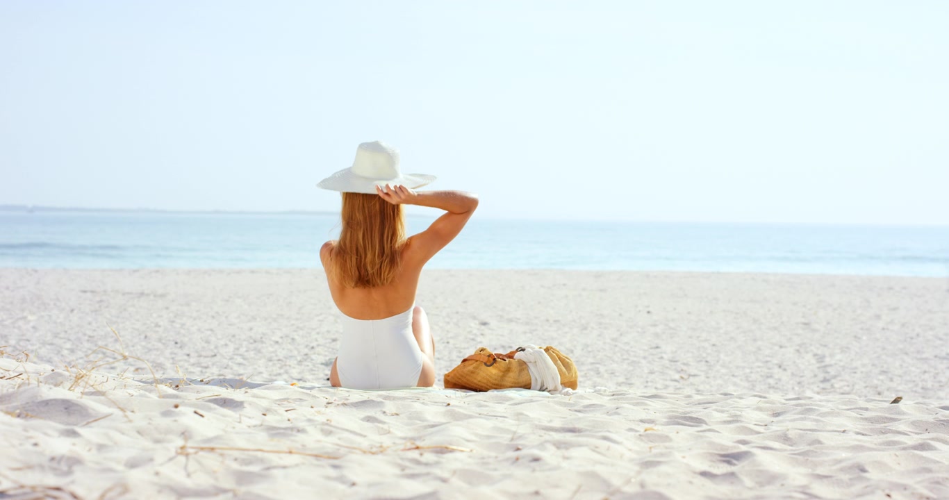 Woman in White Swimsuit Putting on Sun Hat at the Beach