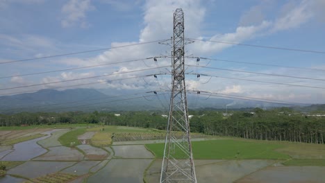 helix drone shot of high voltage electric tower build on the middle of rice field plantation