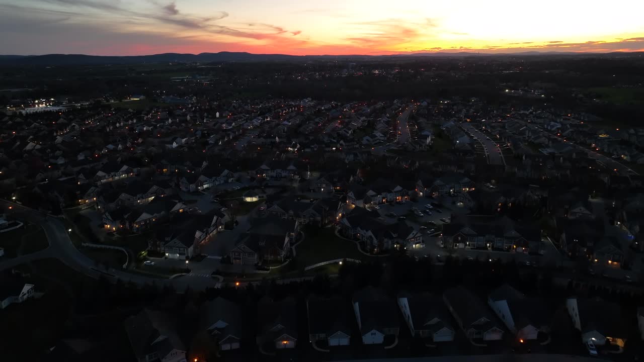 어두운 하늘 아래 집의 불빛이 반이는 광활한 교외 동네 위에 황혼이 가라앉습니다.