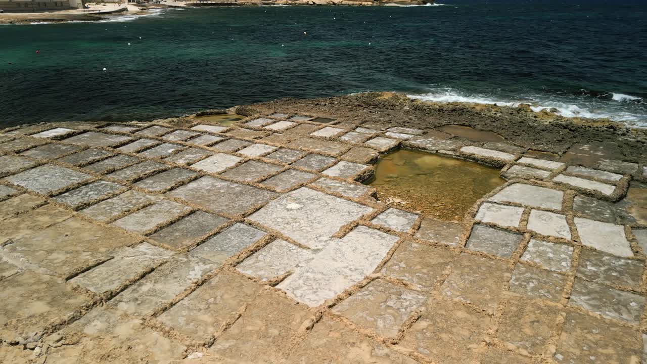 Roterende flyfoto av rektangulære saltpanner med havbølger på kysten av Gozo, Malta