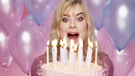 beautiful young woman blowing out candles celebrating birthday pink and blue balloon background - red epic dragon