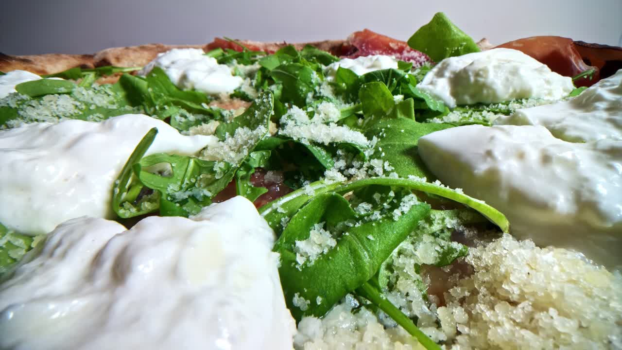Low angle side view of pizza crust with prosciutto, burrata, and arugula