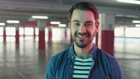 portrait of young caucasian man smiling at the camera while standing in aempty parking