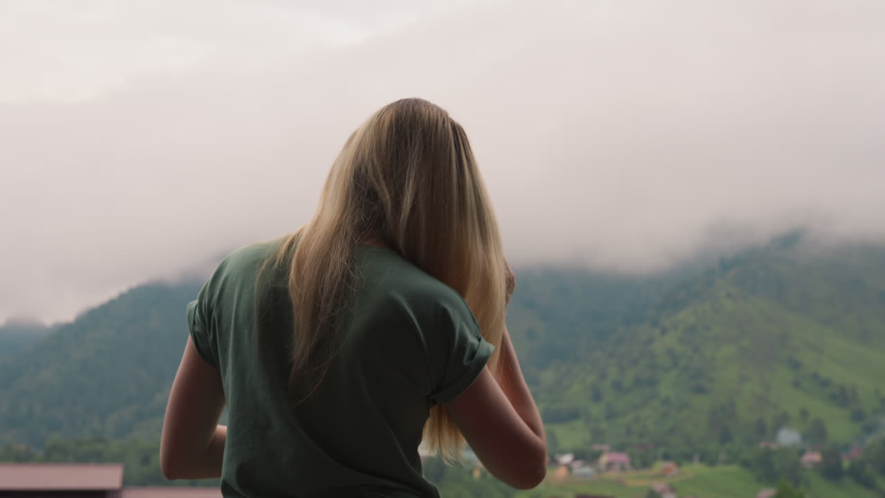 Woman brushes blonde hair standing on balcony of hotel room