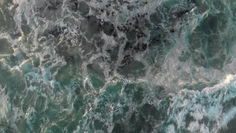 aerial view of wave rolling into frame and following it until it crashes into cliff hill shore